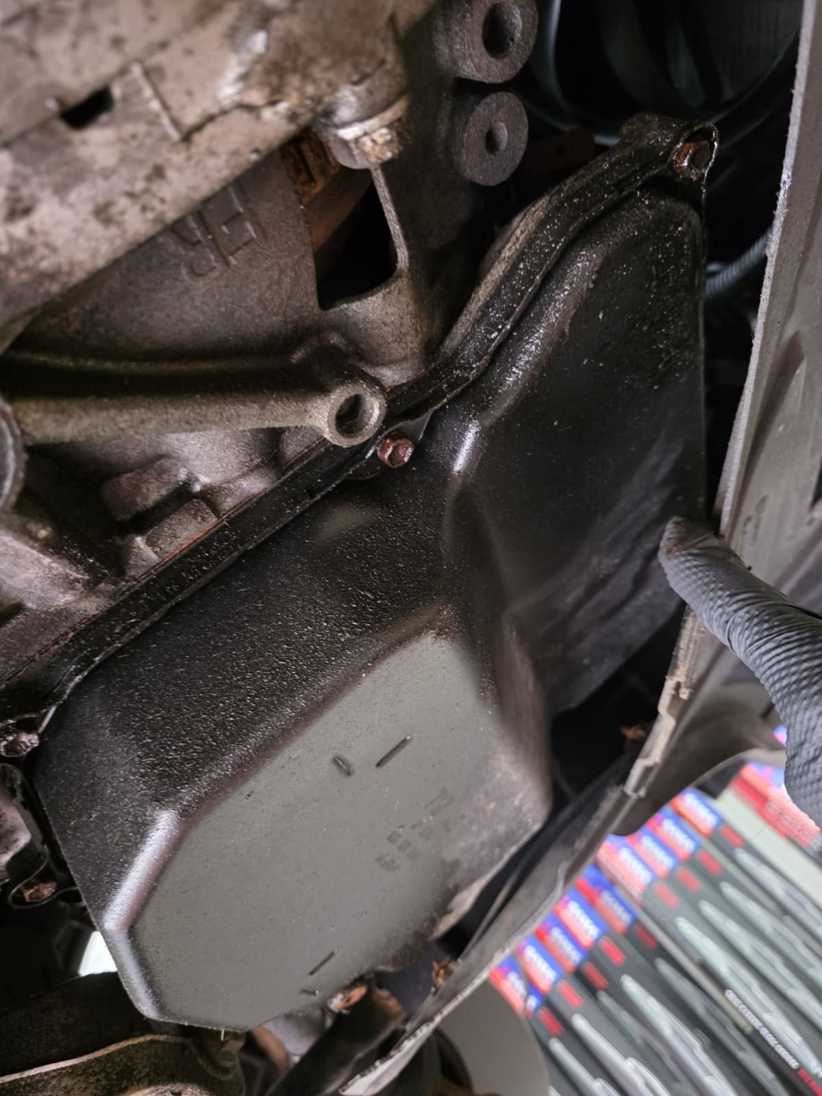 Underside of the transmission, with the pan and its gasket edge wet with fluid