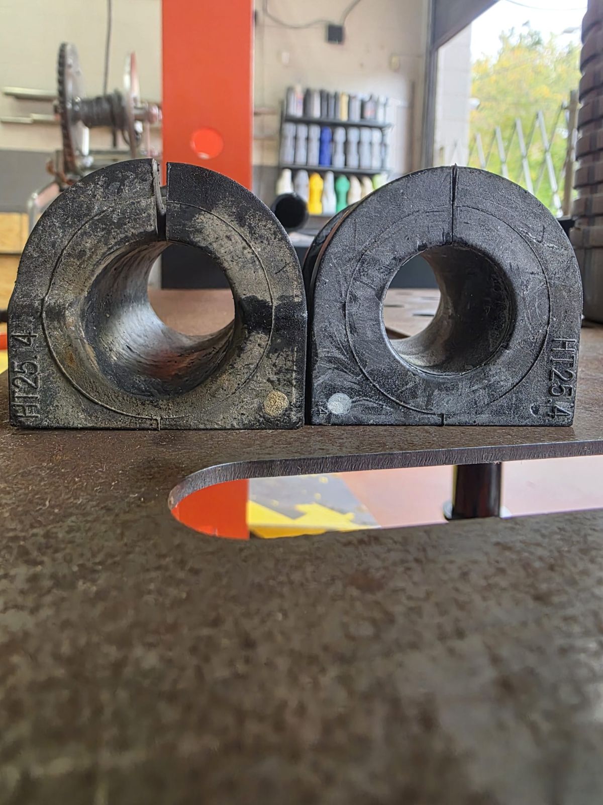 Worn sway bar bushing with a stretched, oval hole beside a new bushing with a round hole