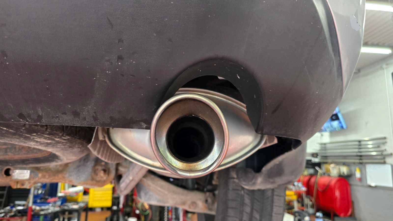 Rear exhaust tailpipe and muffler sitting close against the bumper cutout