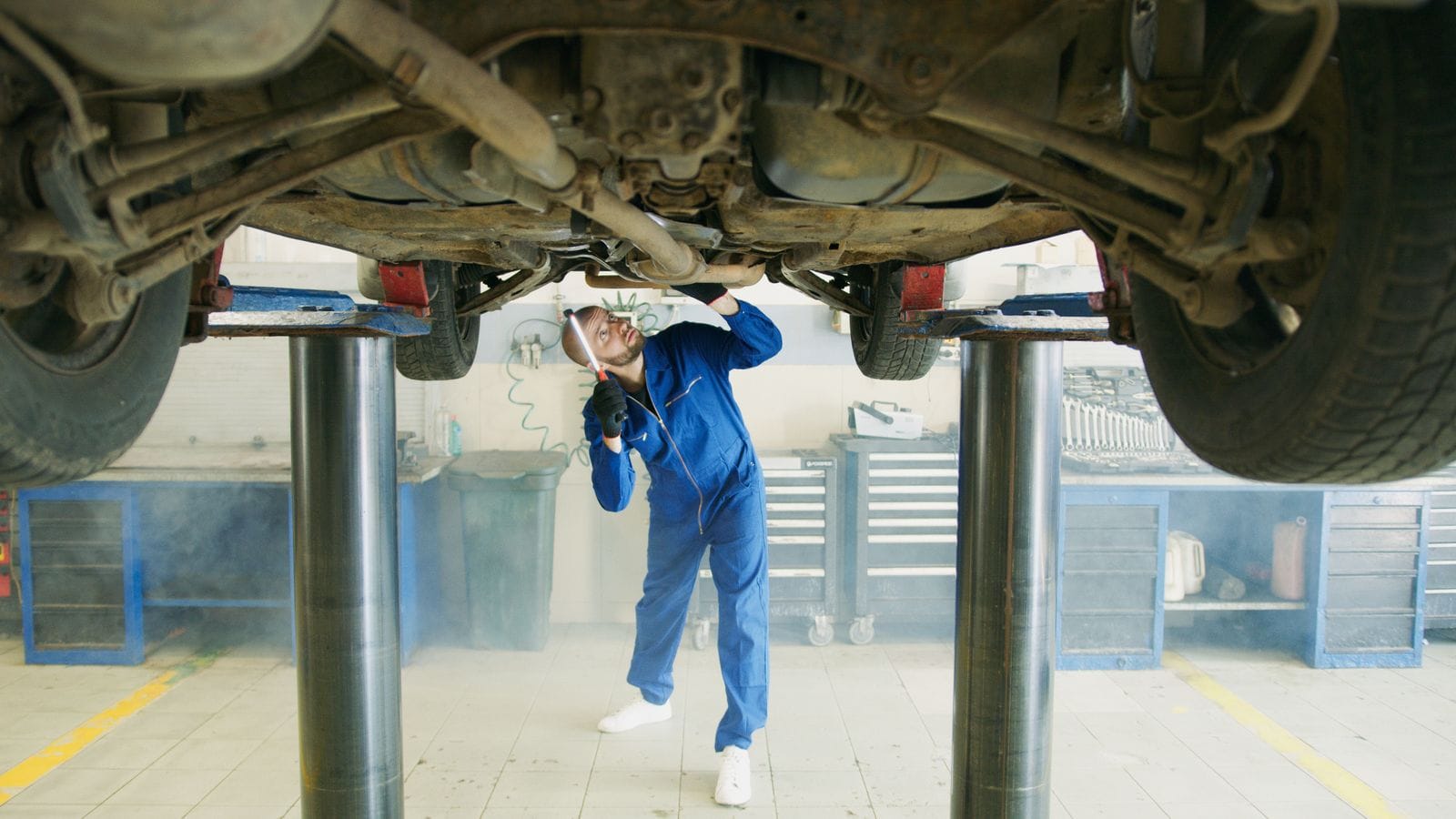 A technician working under a car raised on the shop hoist